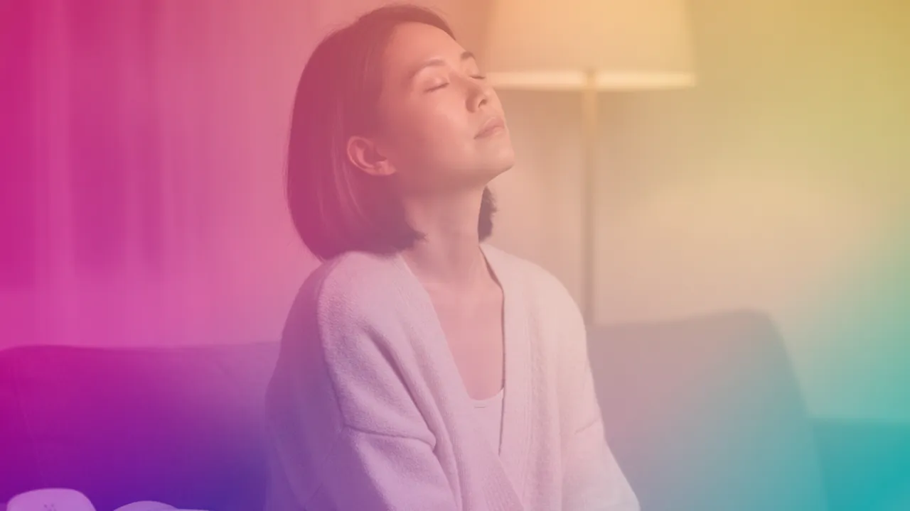 A mother sits on a sofa in a lamplit room in the evening, eyes closed and head tipped back, utterly drained